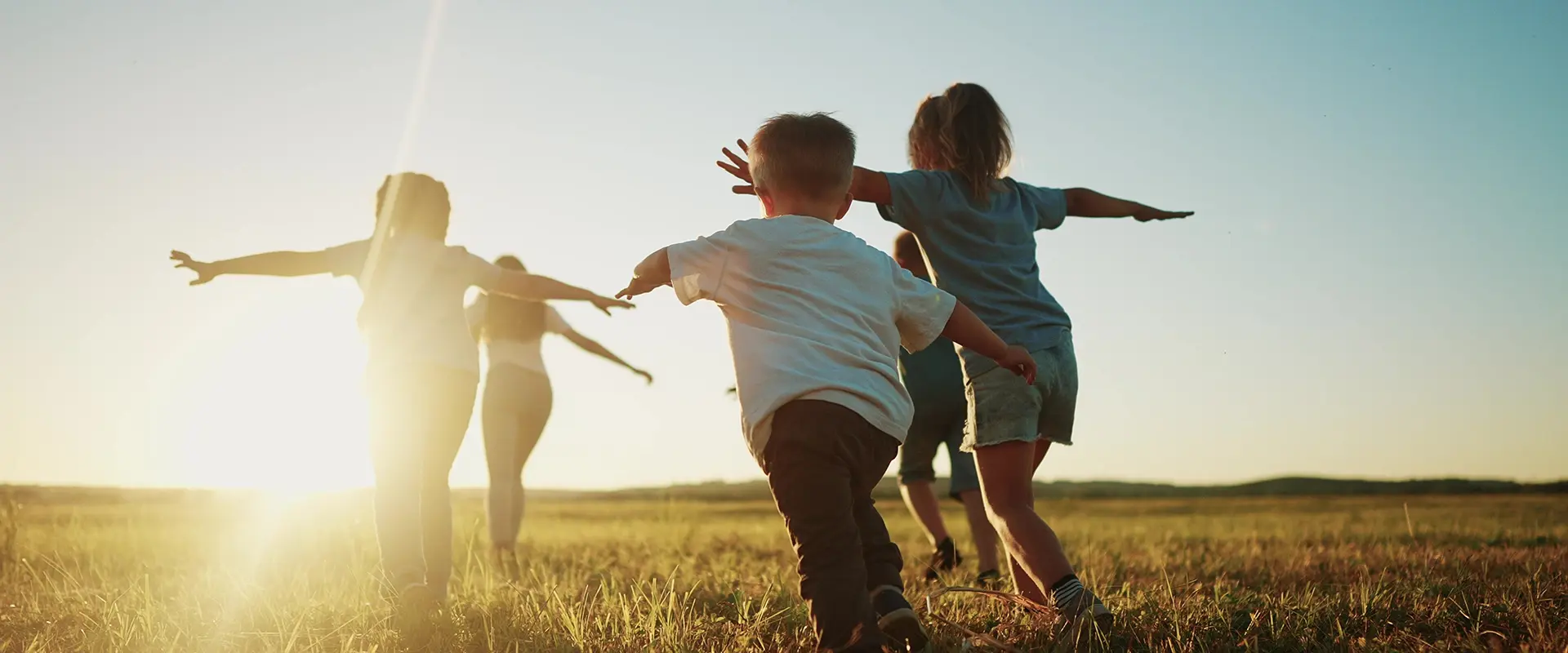 Eine Gruppe Kinder rennt auf dem Rasen im Schein der Sonne.